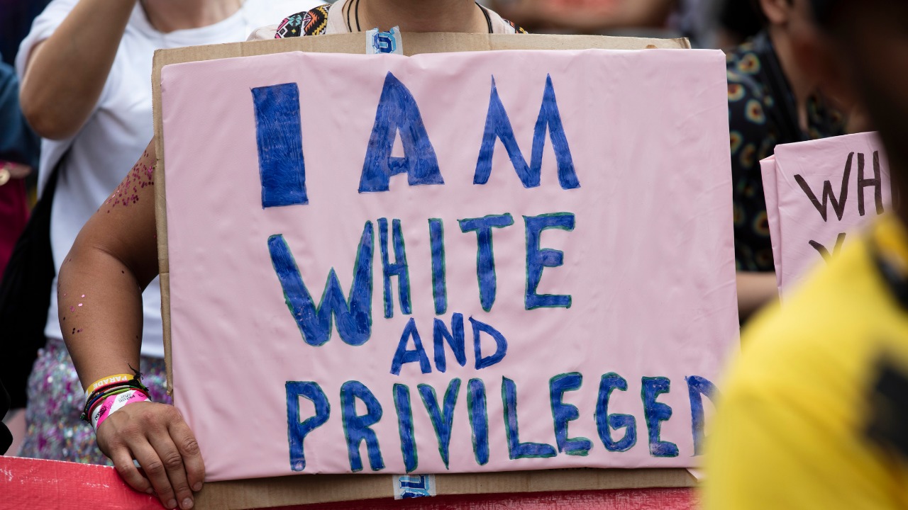 white woman holding a sign that says I am white and privileged